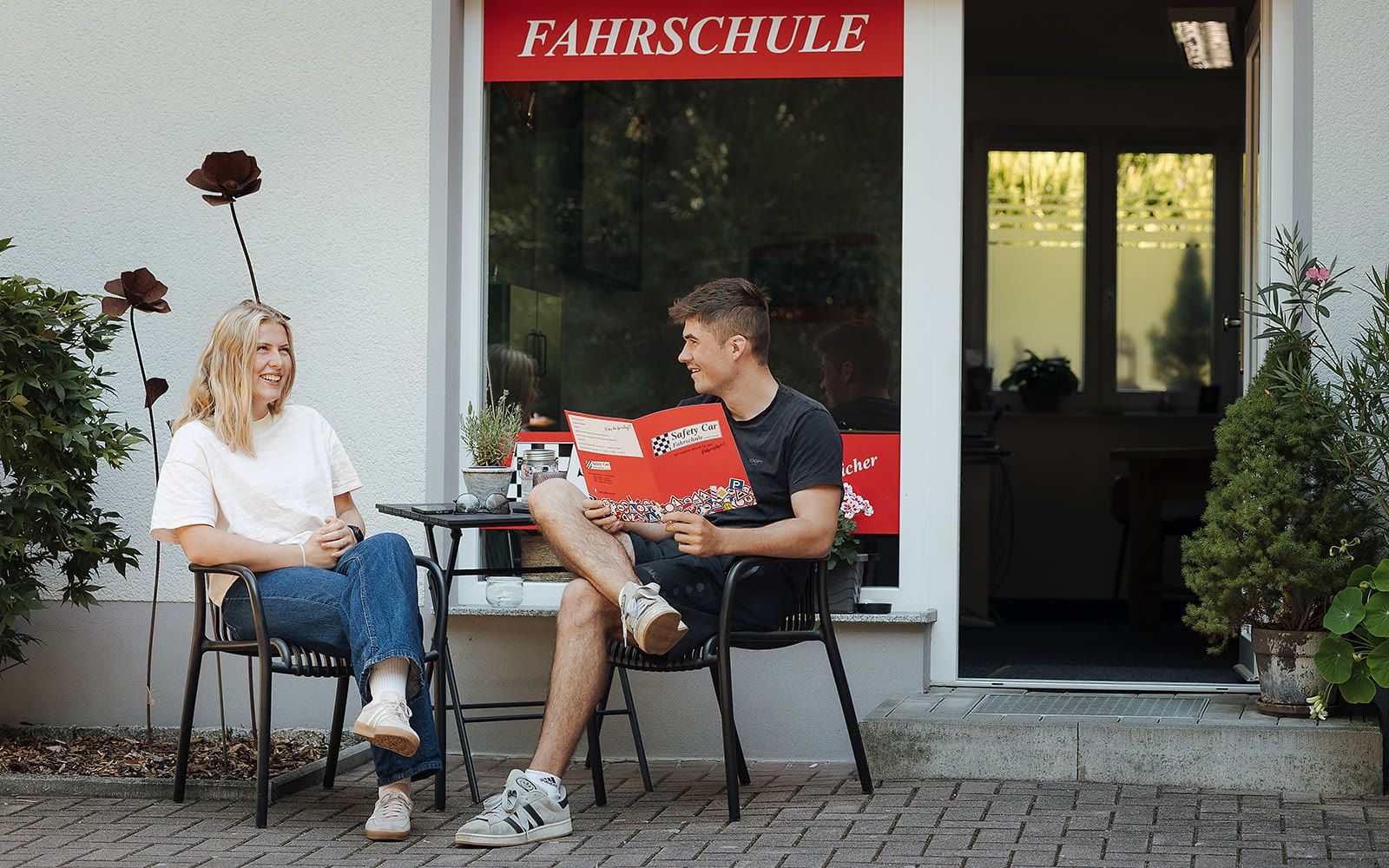 Zwei Fahrschüler sitzen vor der Fahrschule mit Unterlagen zum Ferienkurs
